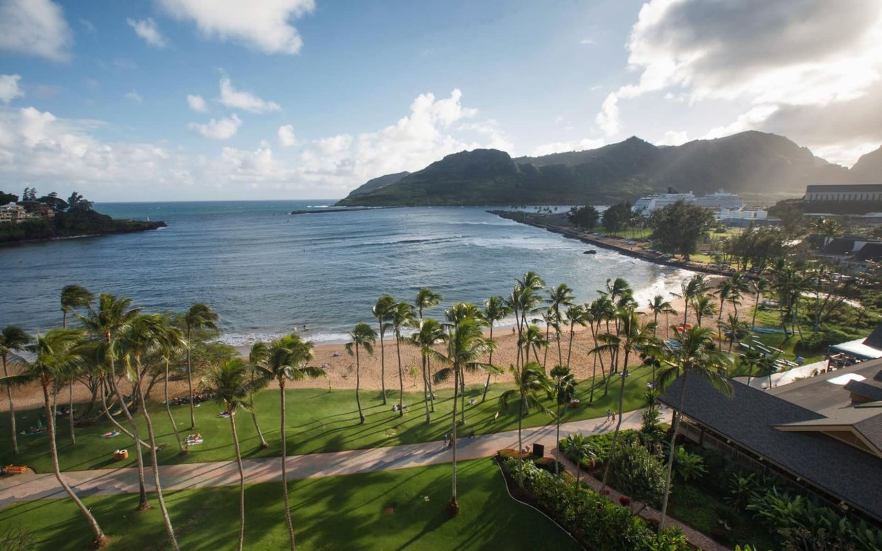 Palm-lined Kalapaki Beach with white sand and turquoise water, resorts nearby, and distant mountain views.