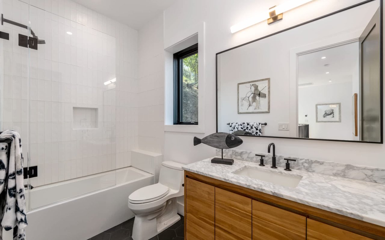 Modern bathroom with a tiled tub, black fixtures, and a wood-front vanity.