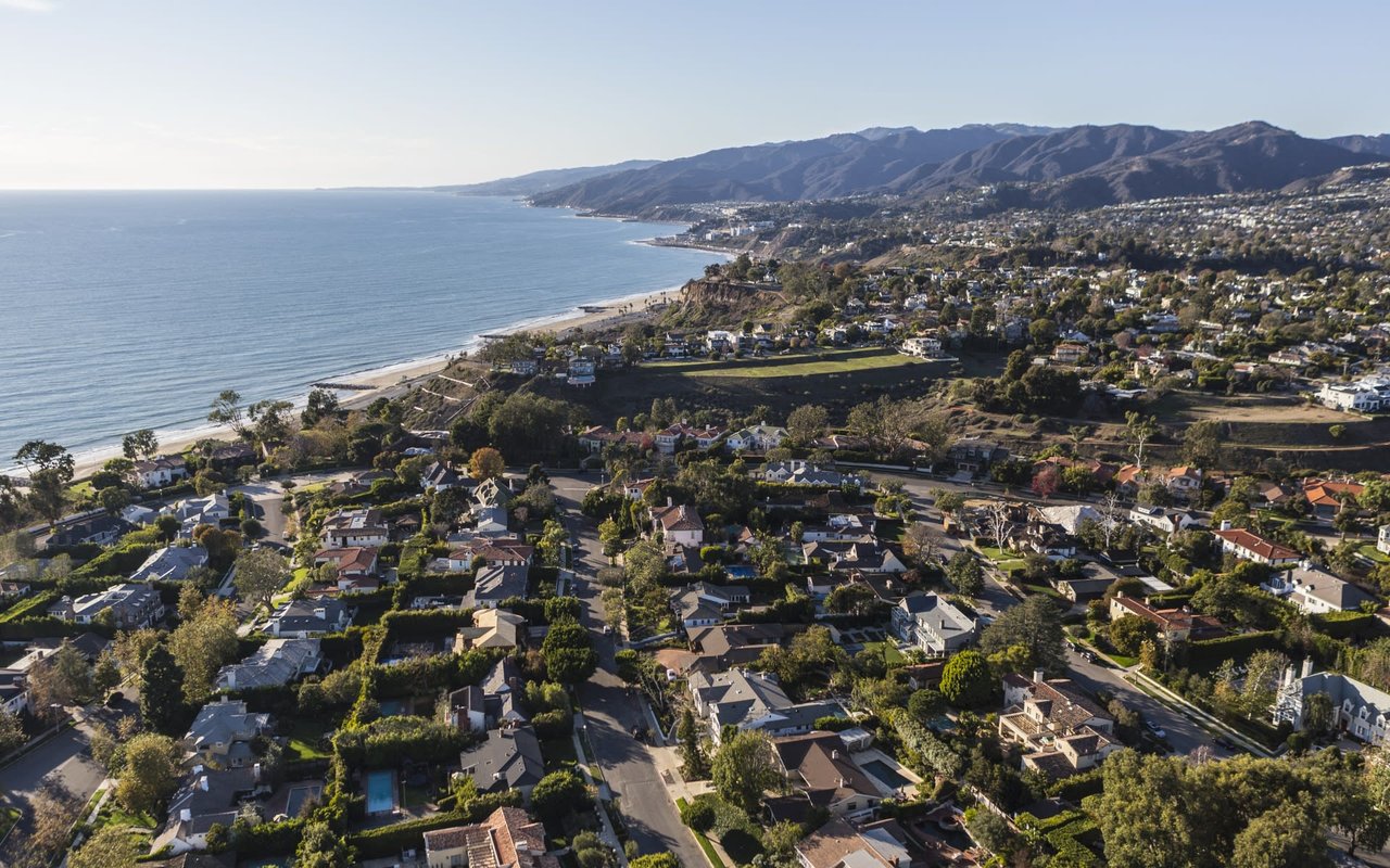 An aerial view of a coastal neighborhood with houses, trees, and blue ocean water.