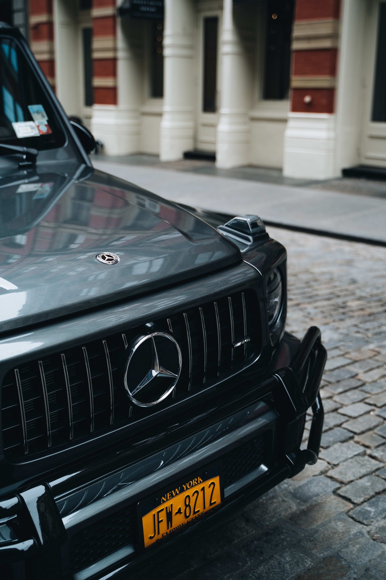 Black Mercedes-Benz SUV with a New York license plate parked on a cobblestone street.