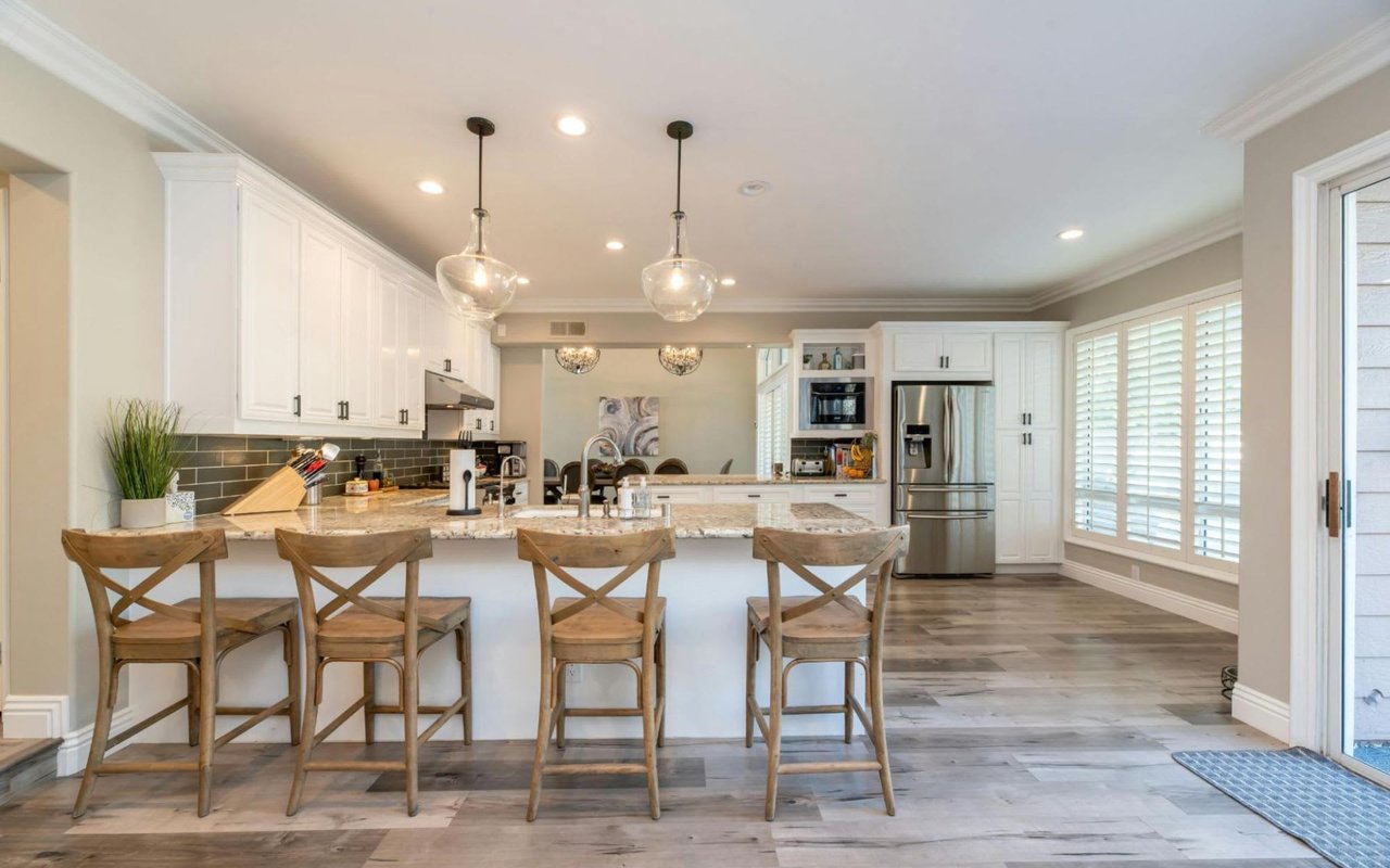 Sleek white kitchen with a spacious island, open to a dining area.