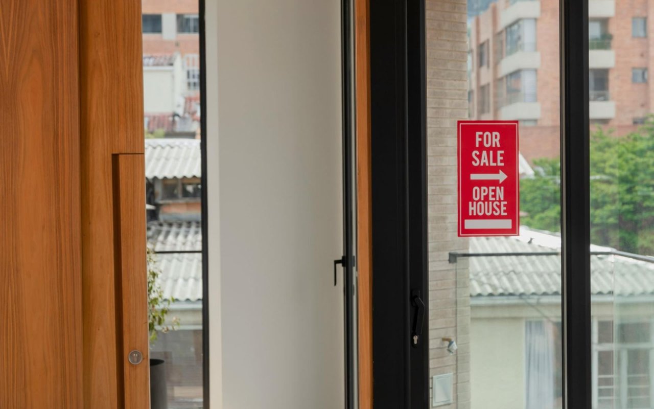 A red For Sale sign with an open house arrow on a glass door.