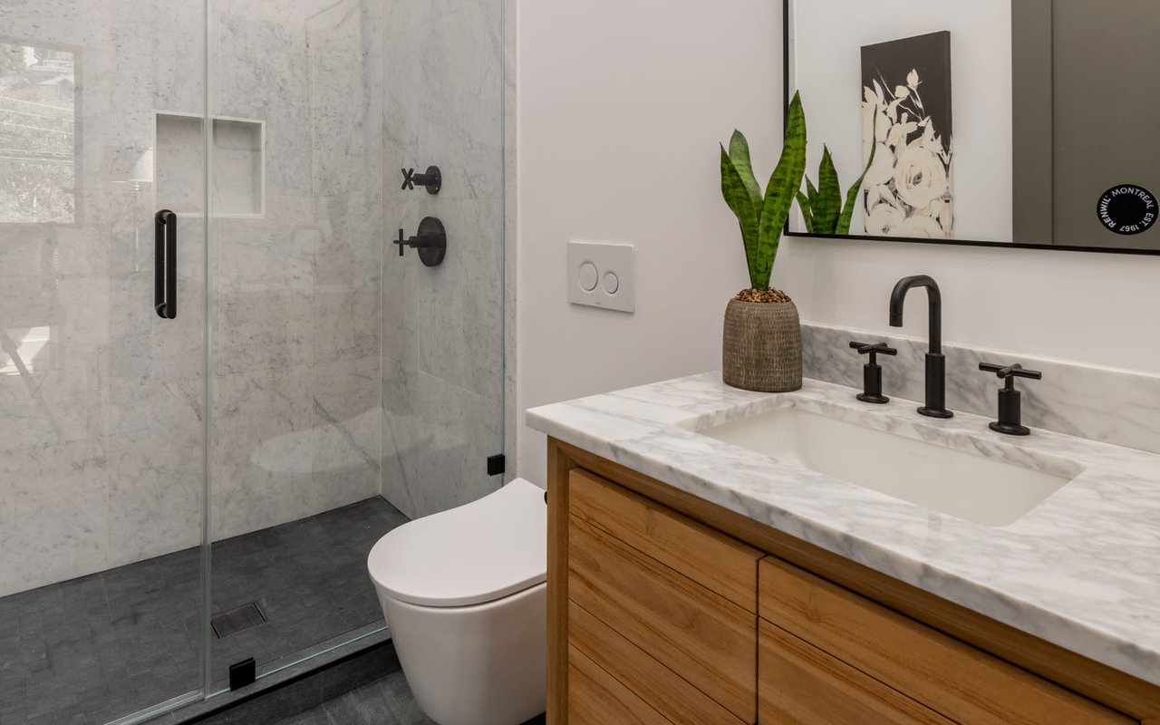 Modern bathroom with a marble shower, glass enclosure, and wood vanity.