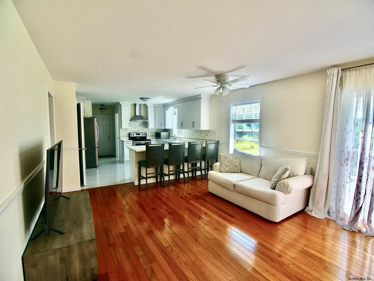 Open-plan living room and kitchen with hardwood floors, a cream sofa, and a breakfast bar.