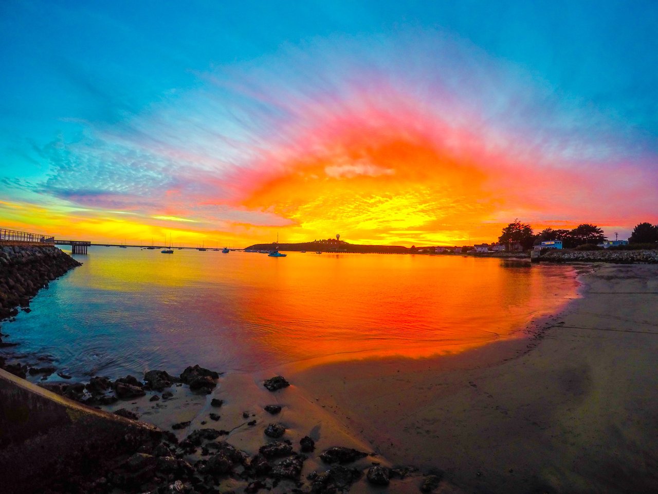 Vibrant sunset over Pillar Point Harbor in El Granada, California, with calm waters, anchored boats, and a view of the iconic radar dome on the coast.