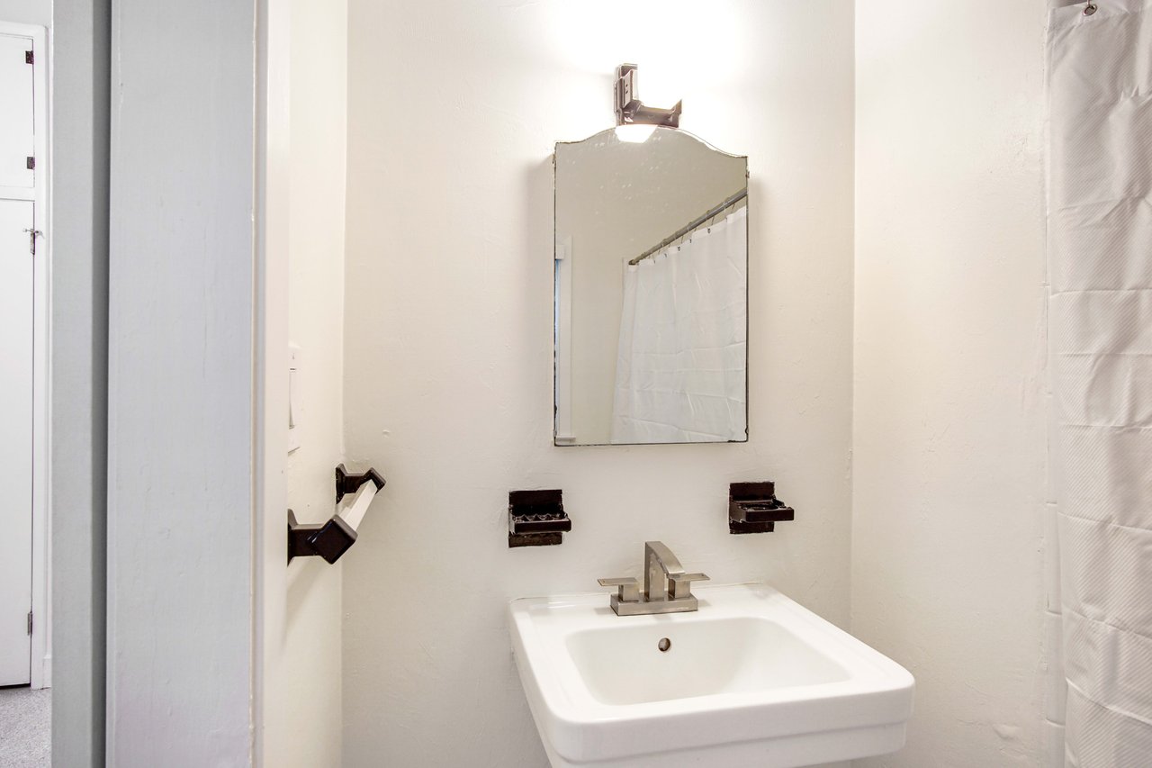 A bathroom featuring a sink with a mirror above it, and modern fixtures. The room has a white shower curtain.