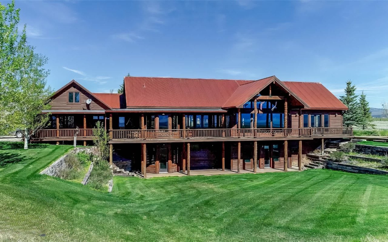 A multi-level house with a red metal roof and dark wood siding, featuring an expansive wooden deck that wraps around much of the structure.