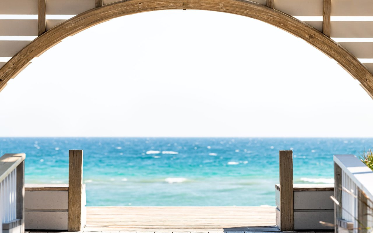 A wooden archway frames a view of a clear blue ocean with whitecaps.