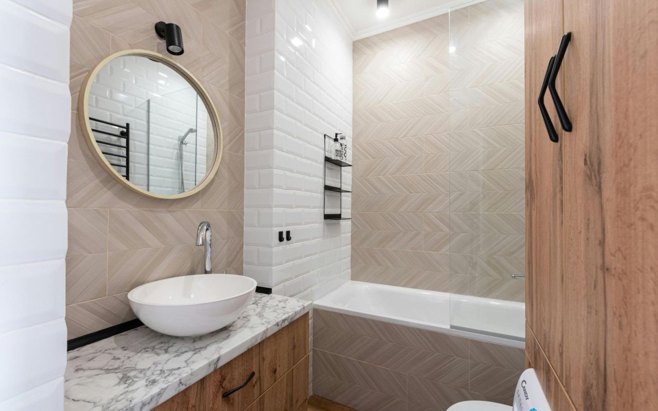 Contemporary bathroom with a round mirror, white subway tiles, marble countertop, and wood vanity.