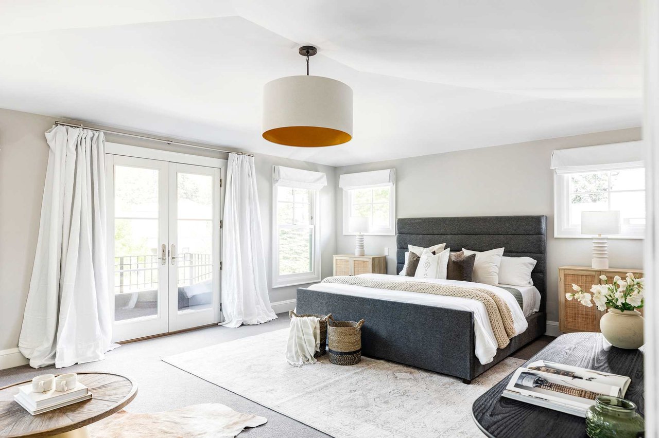 Bright primary bedroom with French doors, white drapes, gray upholstered bed, and natural light