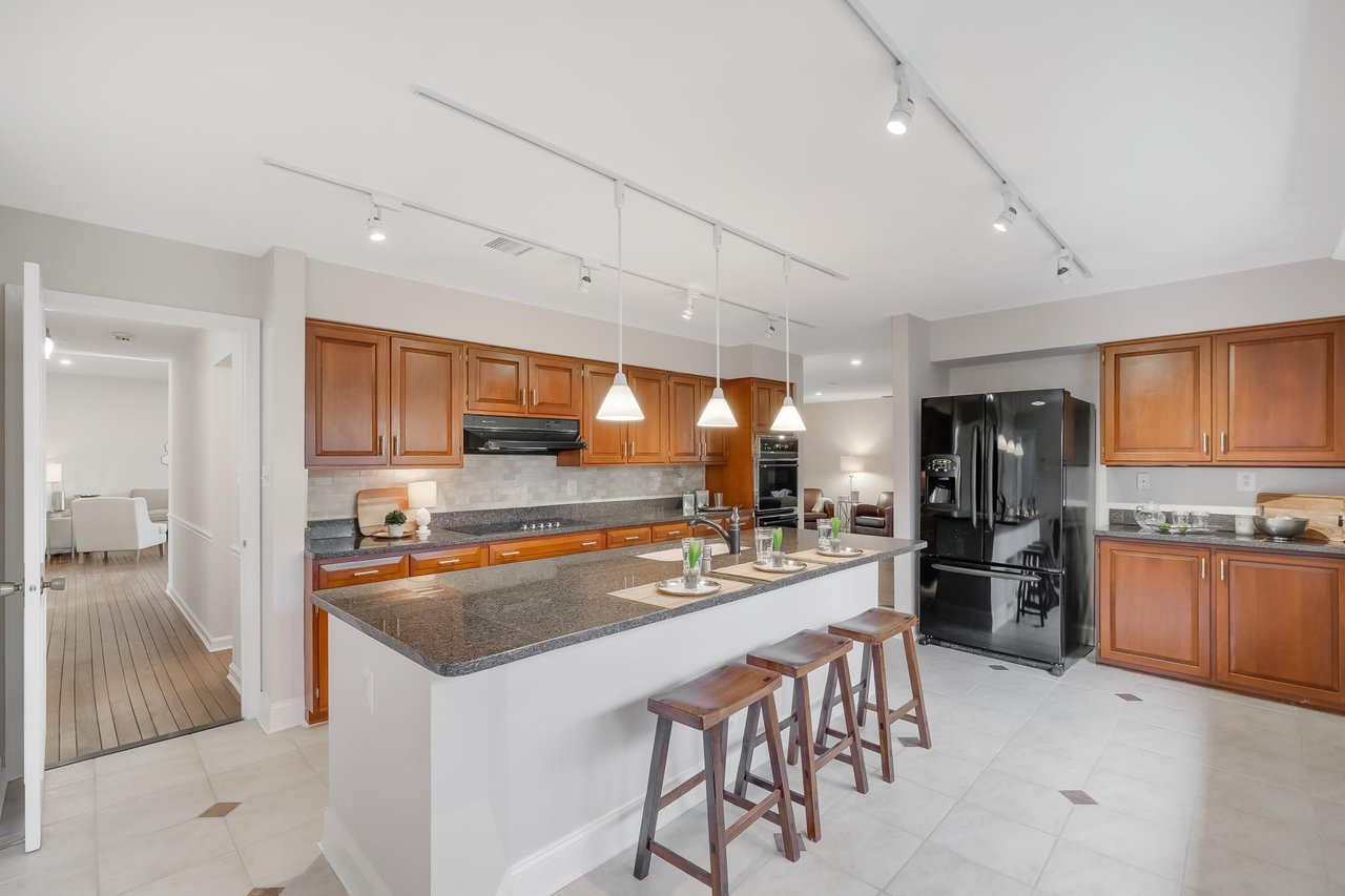 Kitchen with warm wood cabinets, a large granite island, bar stools, and black appliances.