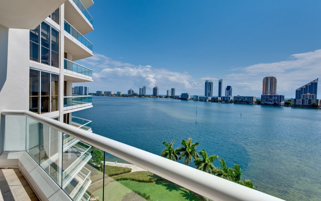 Tranquil balcony retreat with breathtaking ocean views. Palm trees sway against a backdrop of softly glowing urban scenery.