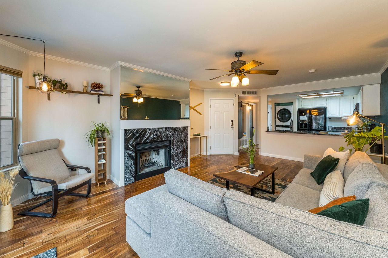 bright open living room with fireplace against the wall and a picture window cut-out that shows the kitchen 