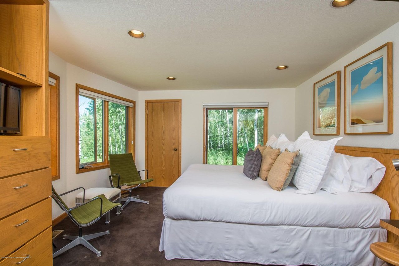 Bedroom with a white bed, wood cabinetry, and windows overlooking trees.