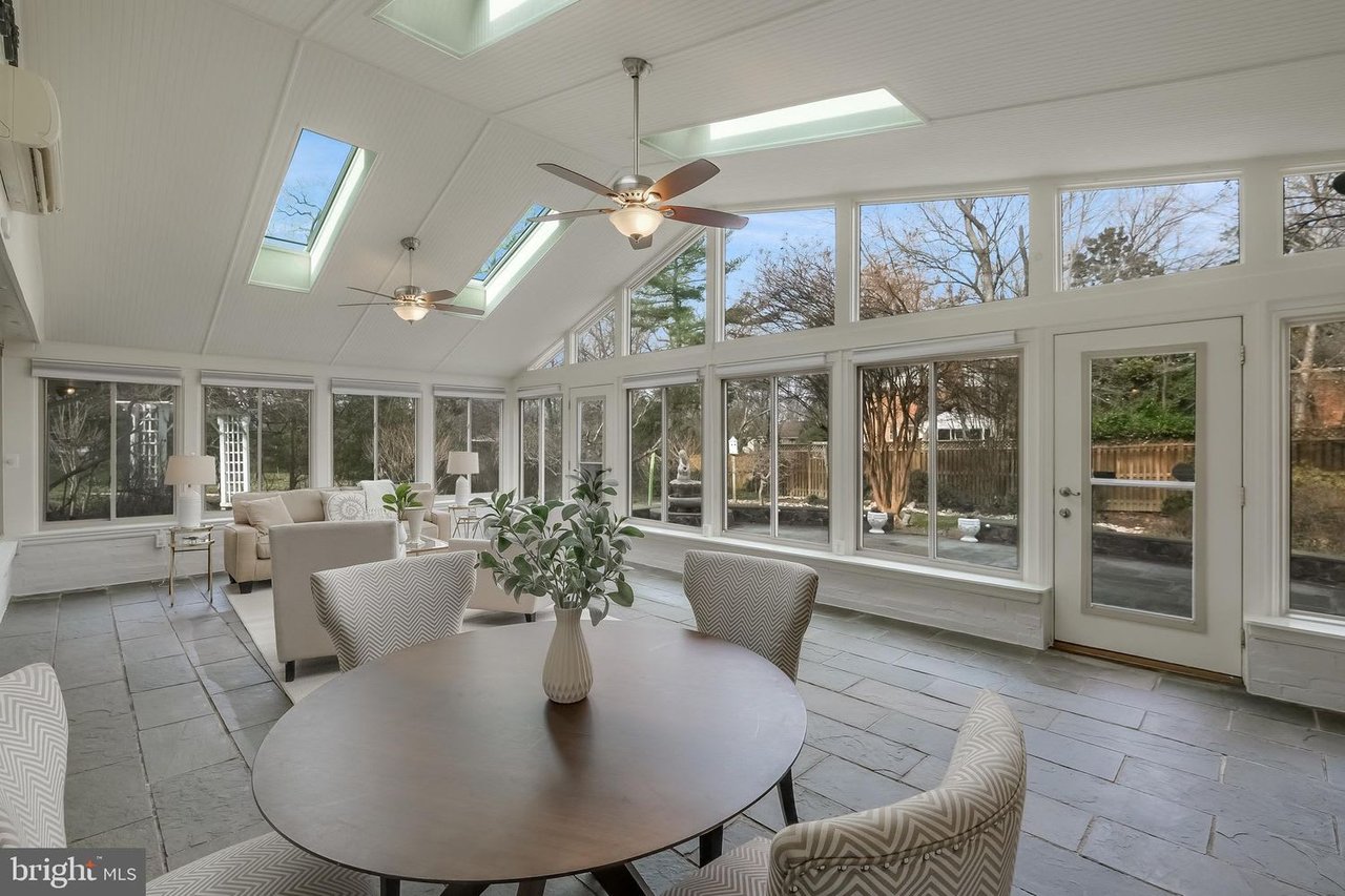 Furnished sunroom with skylights, ceiling fans, and windows overlooking a fenced yard.
