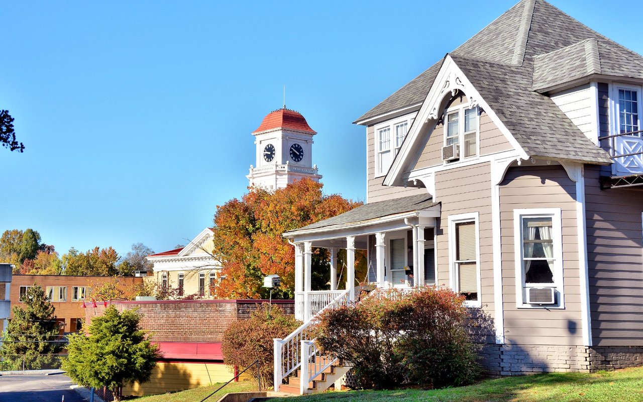 A house with a porch in the foreground and a clock tower in the background.