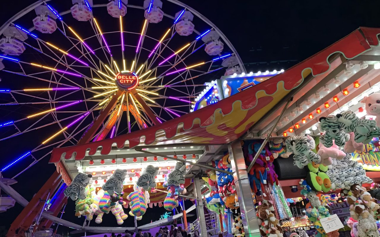 A brightly lit Ferris wheel dominates a carnival scene, with game booths and colorful prizes.