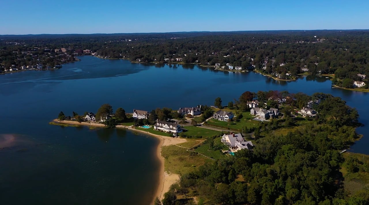 An aerial view of a community beside a lake. The town is forested, with a few houses nestled among the trees.