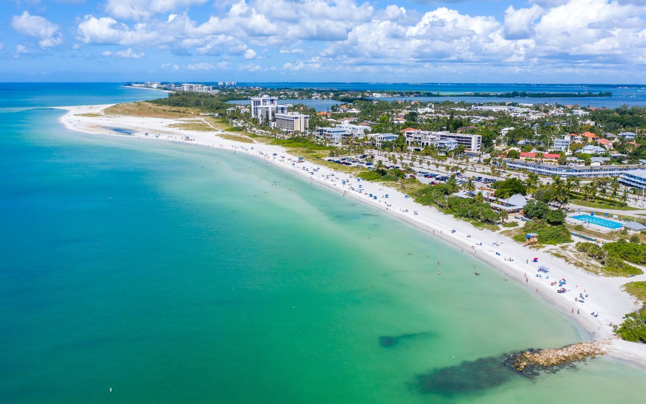 An aerial view of a long beach with high-rise buildings in the background.