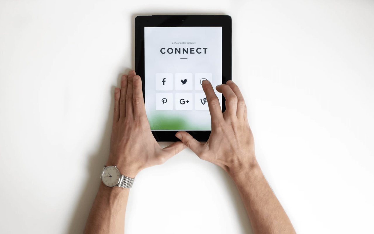 Hands tap social media icons on a tablet displaying “CONNECT.”
