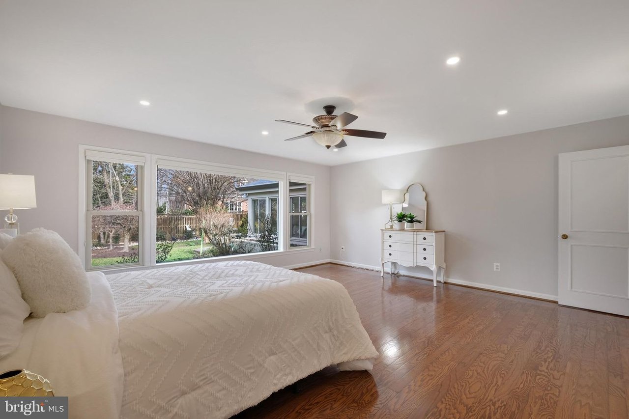 Bedroom with a large bed, broad backyard-facing windows, hardwood floors, and a ceiling fan.