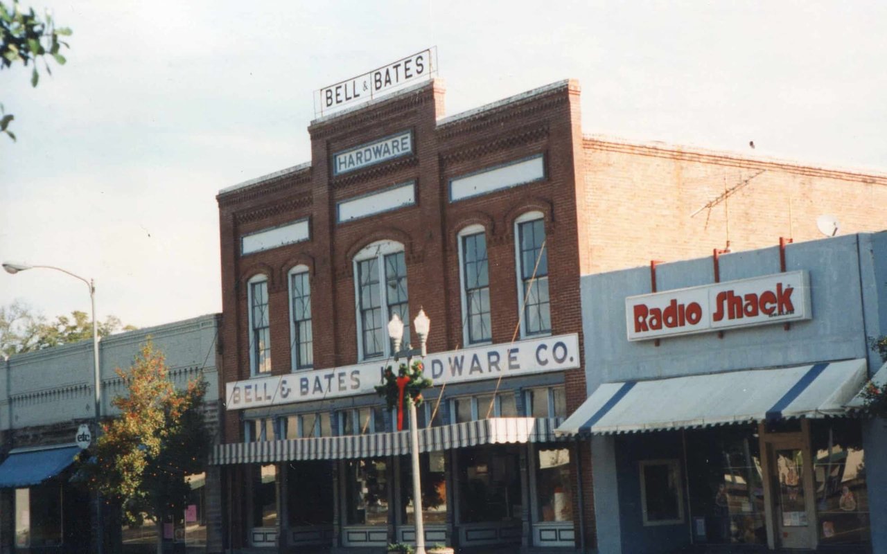 A small town street with a hardware store and a Radio Shack. The buildings have a rustic, old-fashioned look, reflecting the character of a small community.