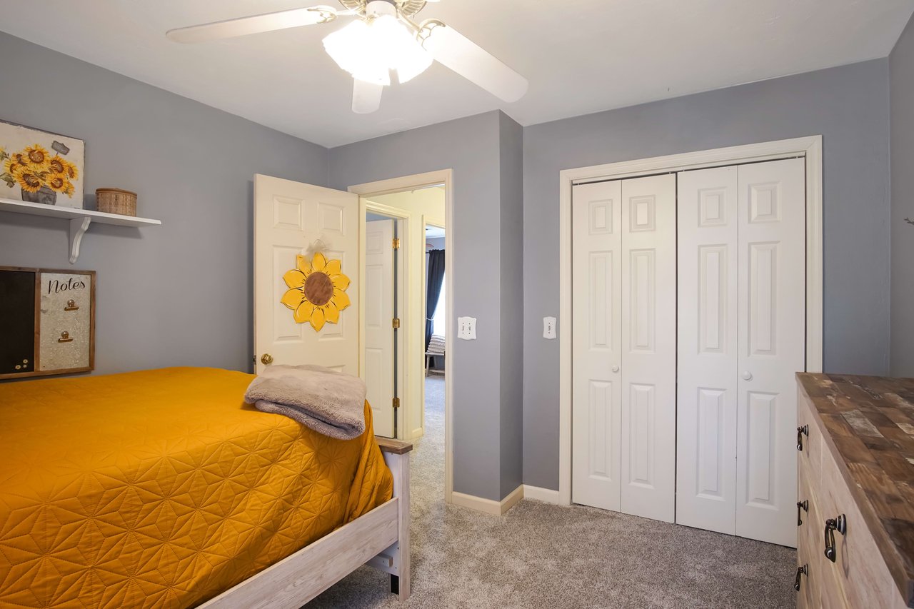 Another interior shot of a bedroom with a yellow bedspread, blue walls, and wooden furniture. The room has a closet with white doors and various decorations.