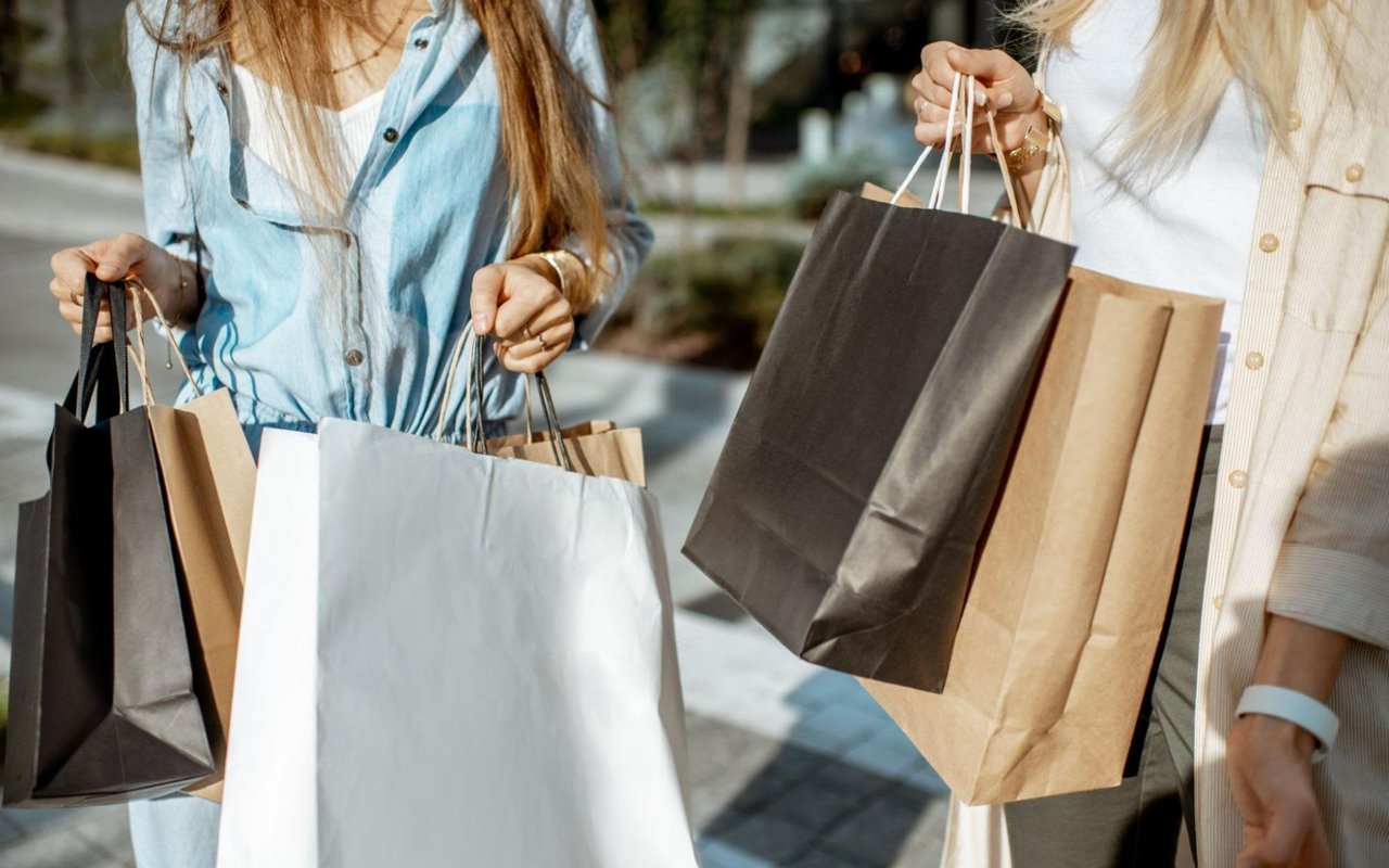 Two women holding shopping bags, walking on a street with buildings in the background.