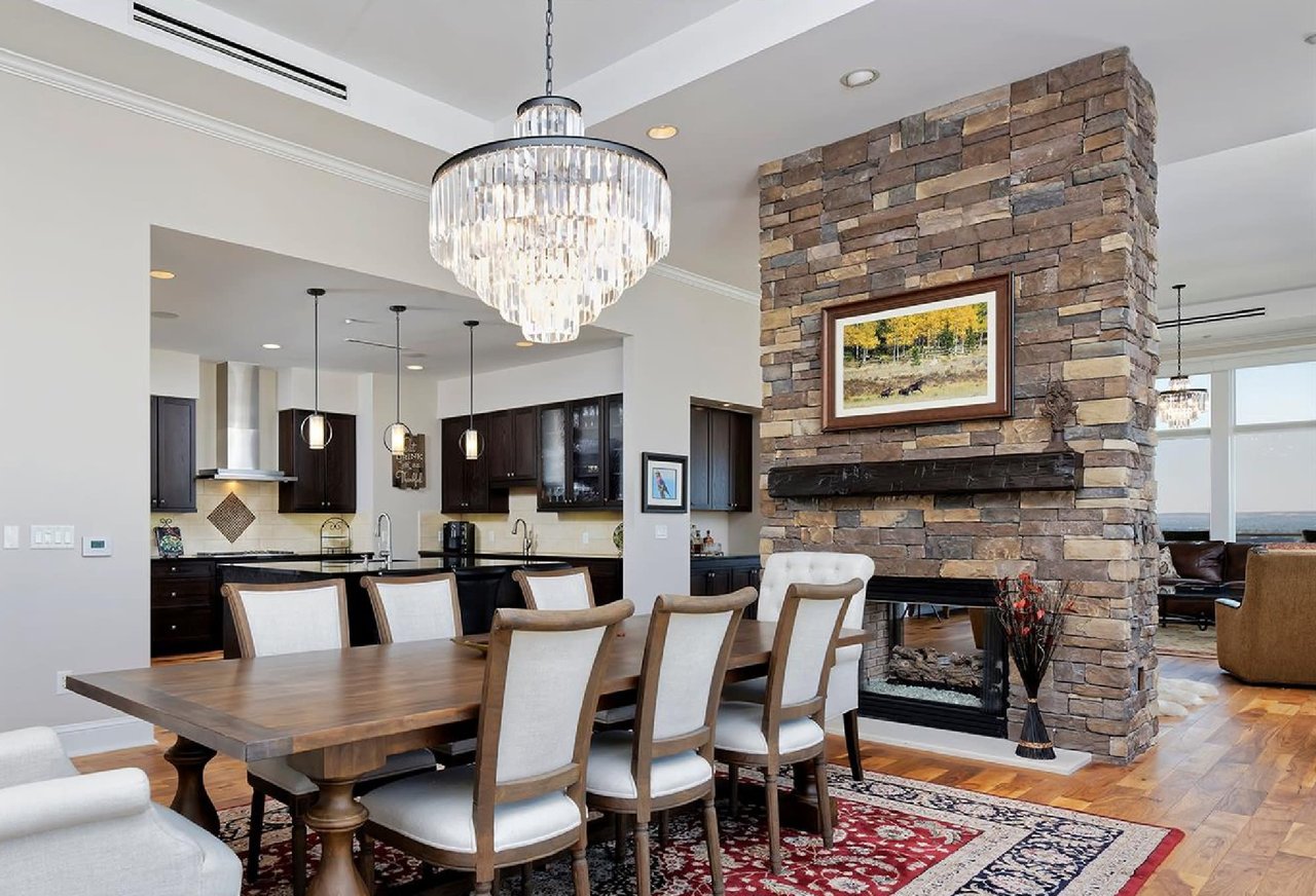 A dining room with dark wood table and chairs, a stone fireplace, a wrought iron chandelier, and nature-themed décor.