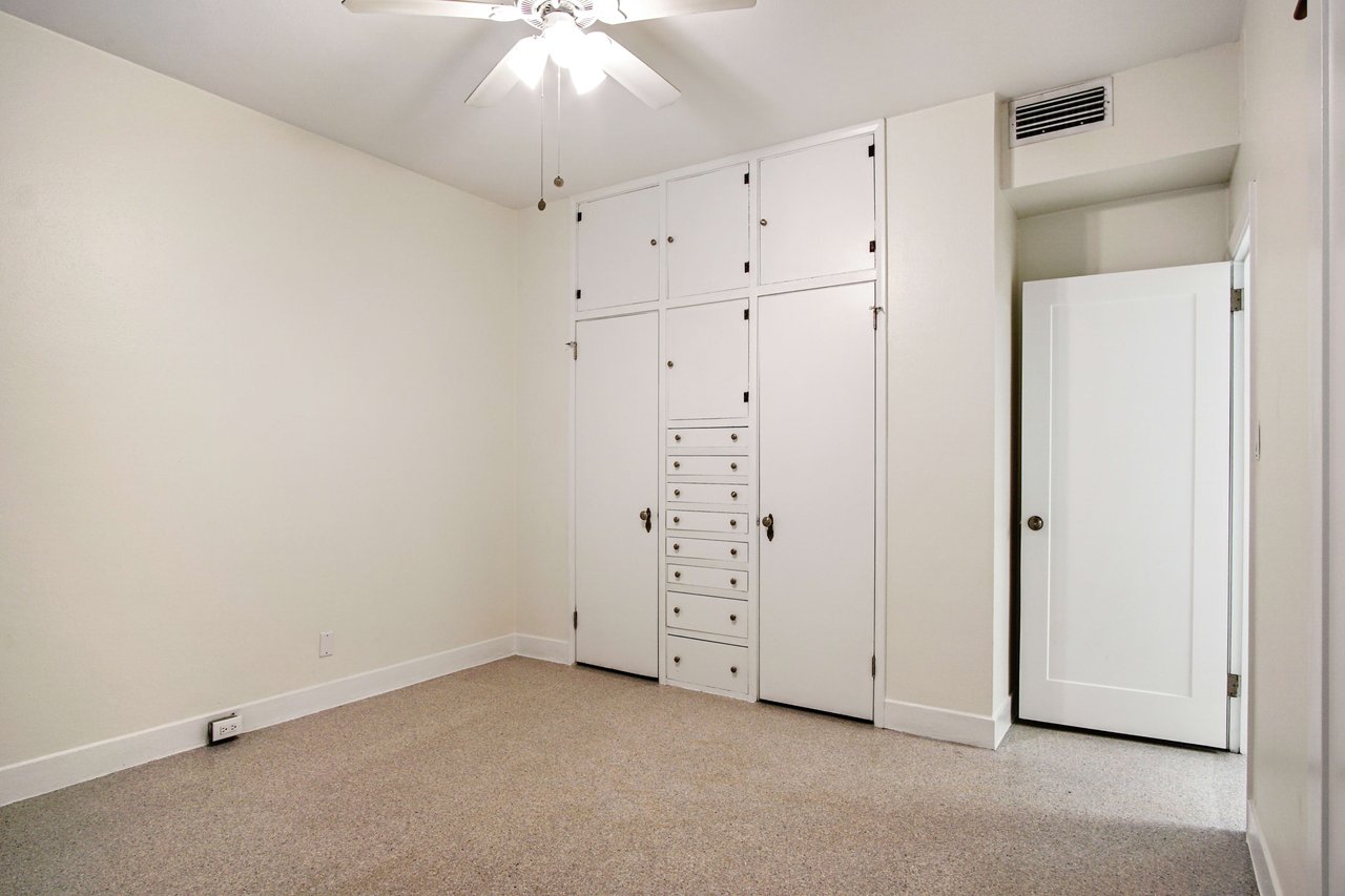 An interior shot of the primary bedroom. The room features built-in storage and a closet, with a neutral color palette and carpeted floor.