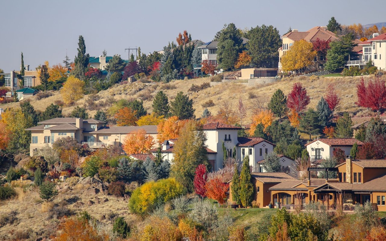 A residential hillside is densely packed with houses featuring varying architectural styles, primarily visible through a vibrant display of autumn foliage.