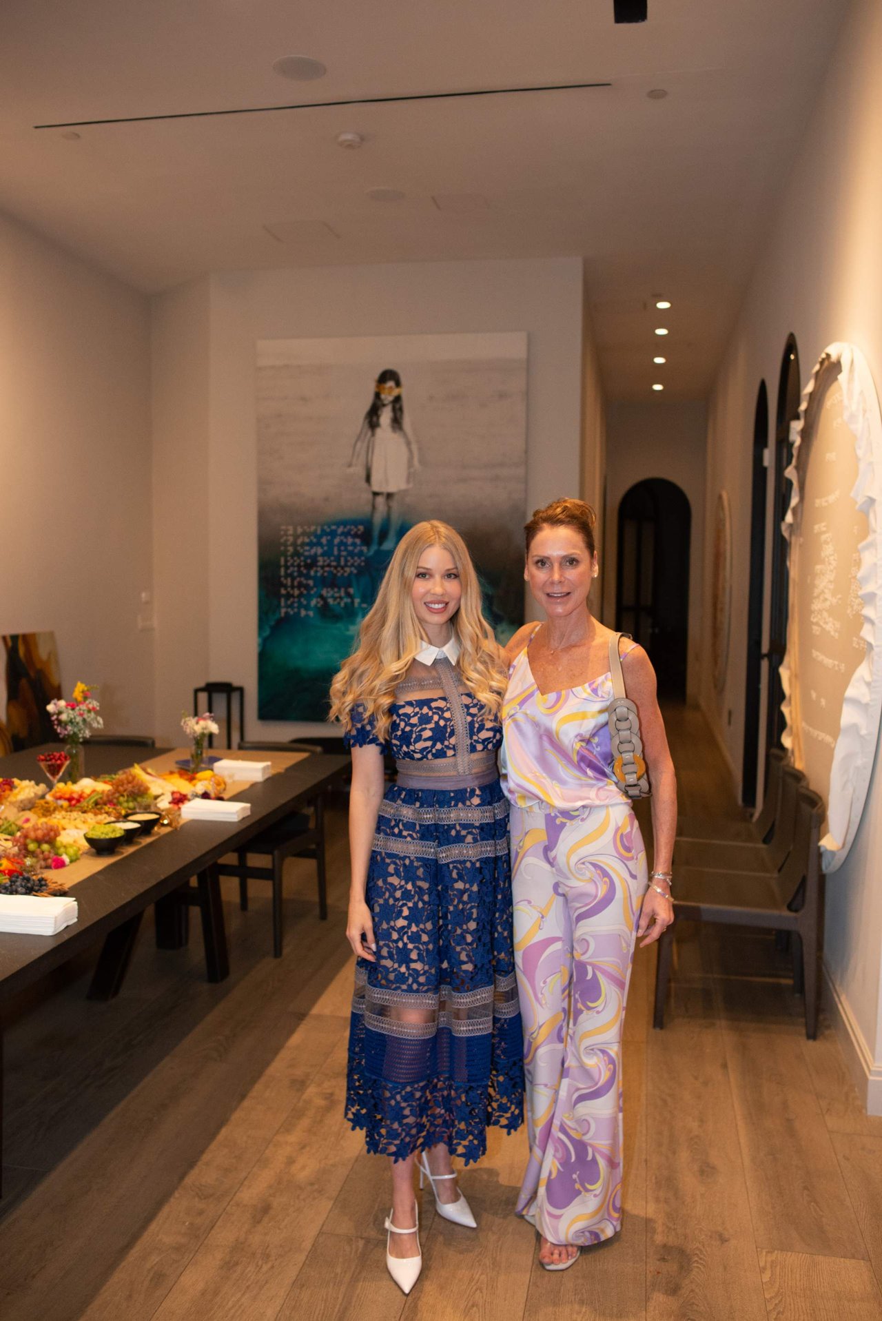 Two women pose together at an indoor event beside a buffet table.