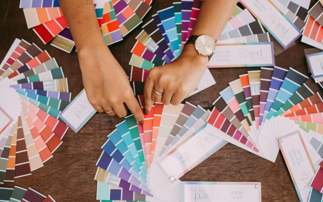 Hands holding a color swatch fan, surrounded by various color swatches on a wooden table.