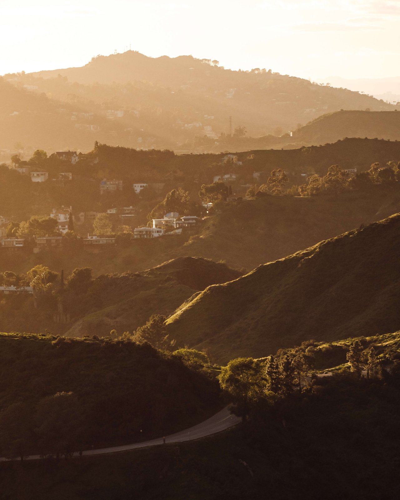 An aerial view of the hills, the sun is setting, casting a warm glow over the hills and the houses below