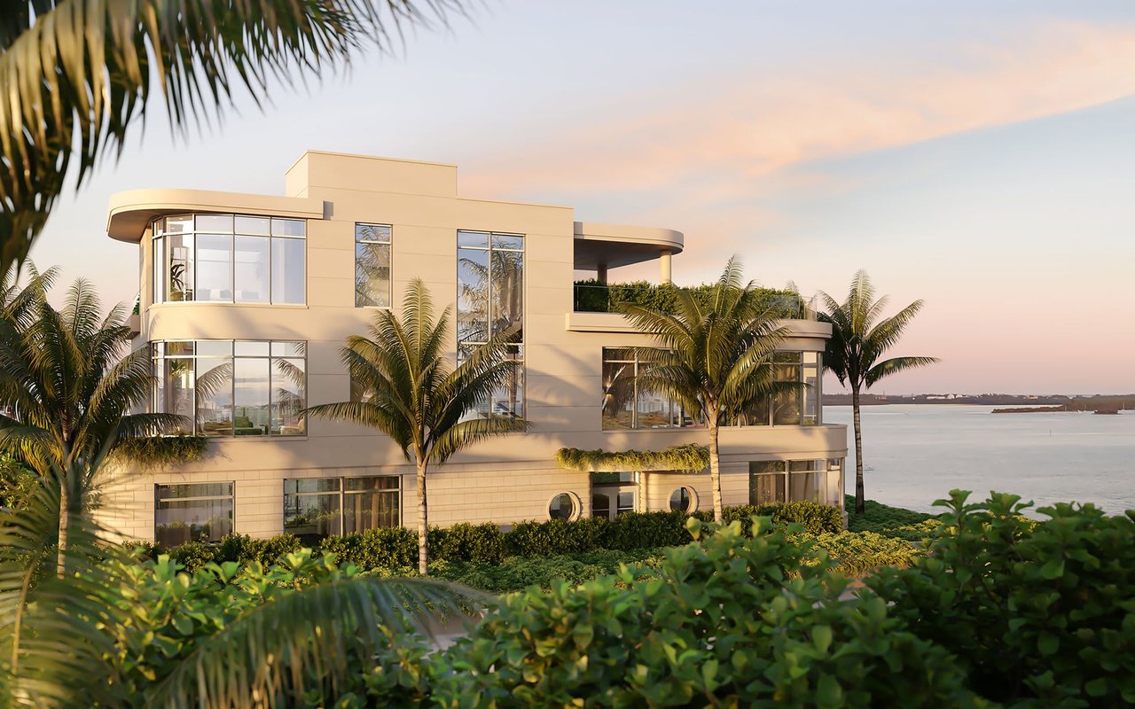 Modern waterfront residence with glass windows, palm trees, and landscaped grounds beside the water.