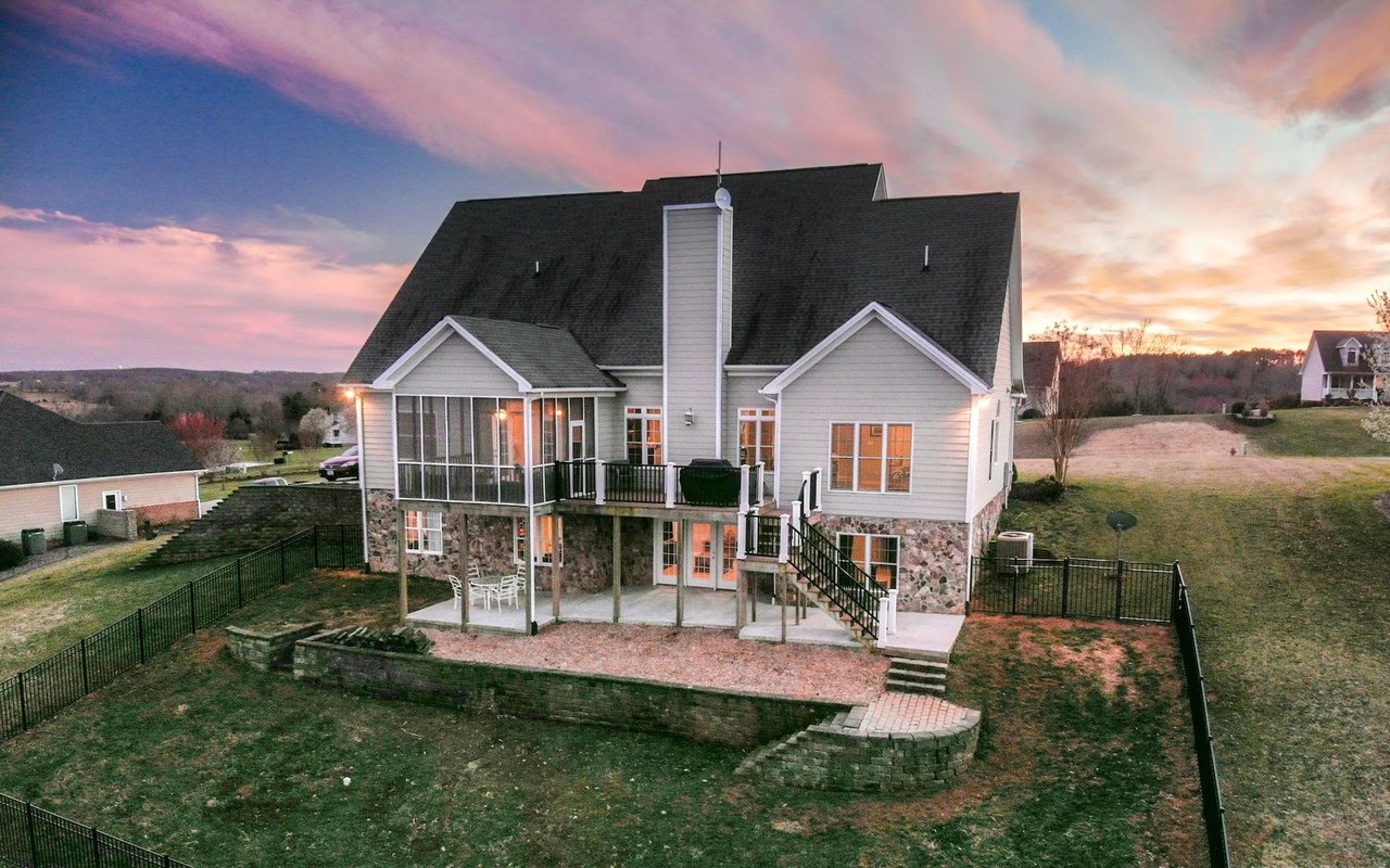 Gray two-story home with a screened porch and fenced backyard beneath a pink dusk sky.