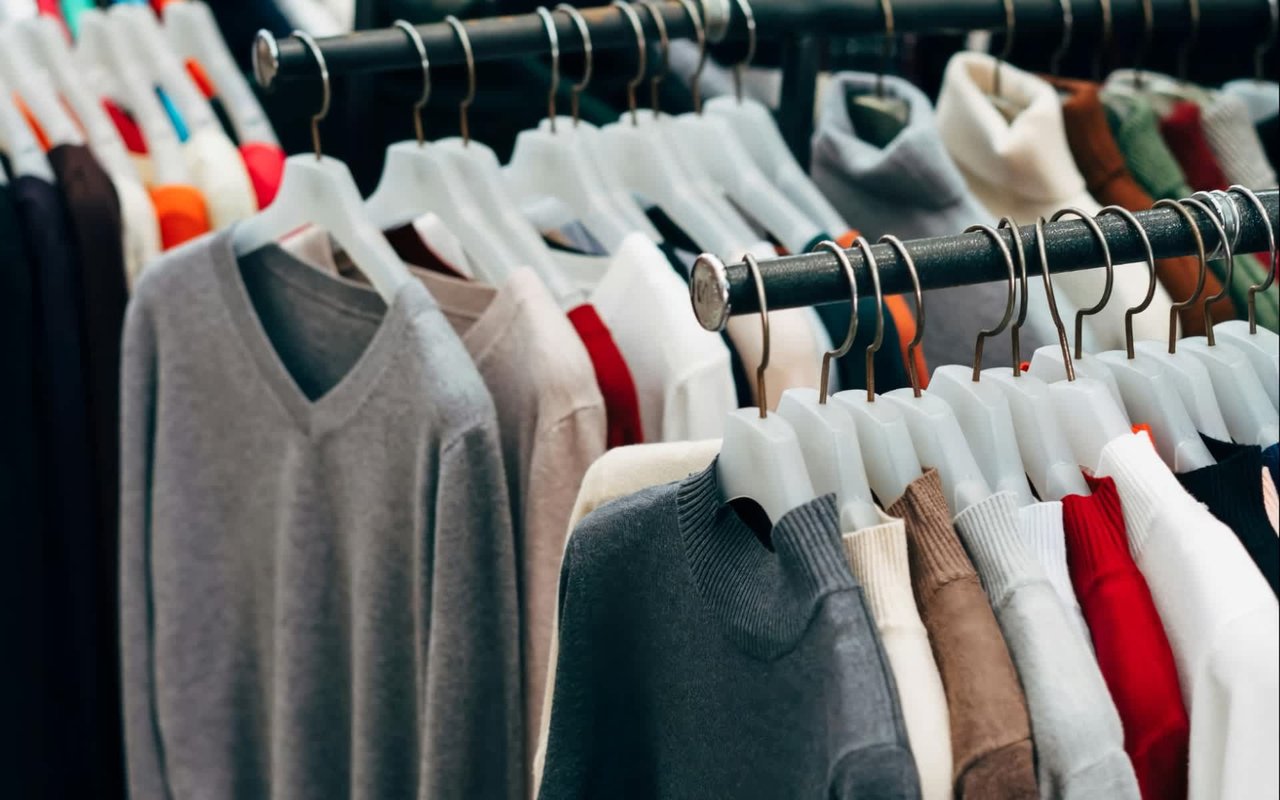 A full clothing rack filled with a variety of sweaters and long-sleeved shirts in different colors and textures