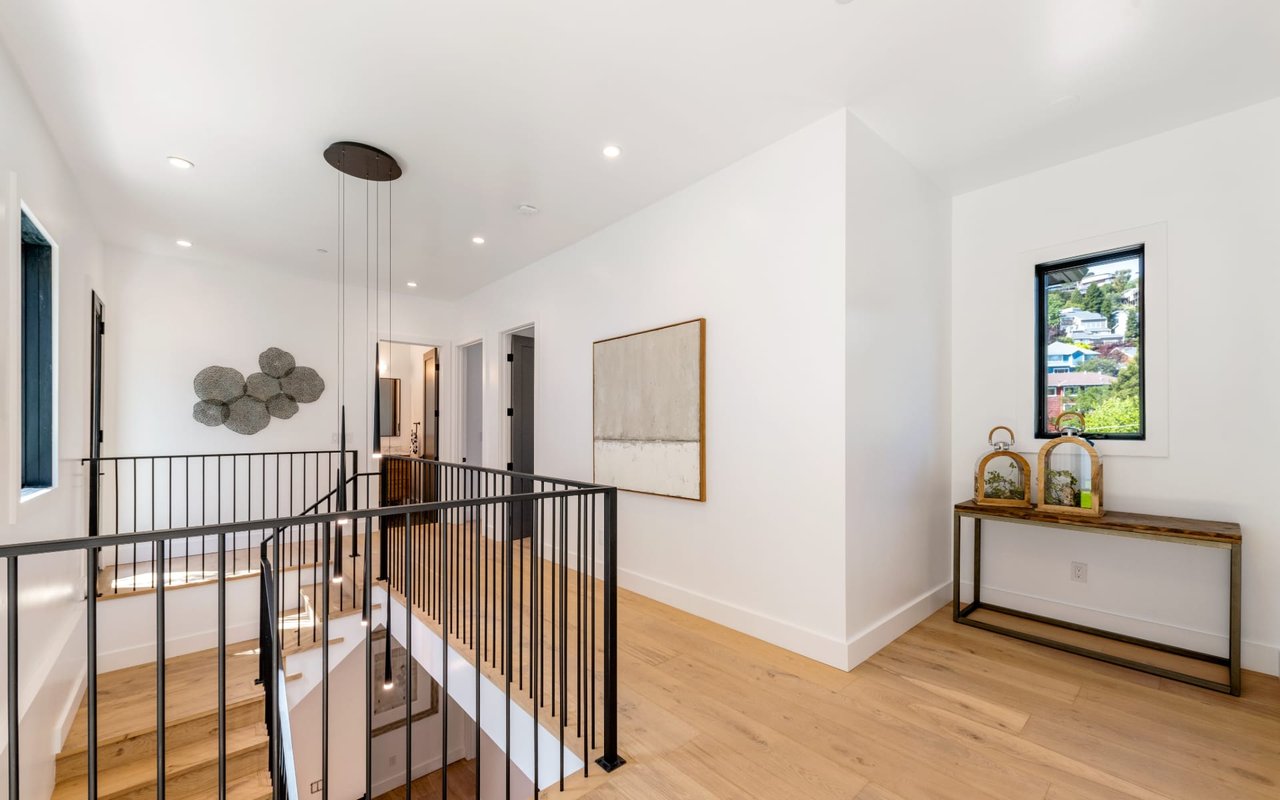 Bright upstairs landing with light wood floors, black railings, and a console table beside a window.