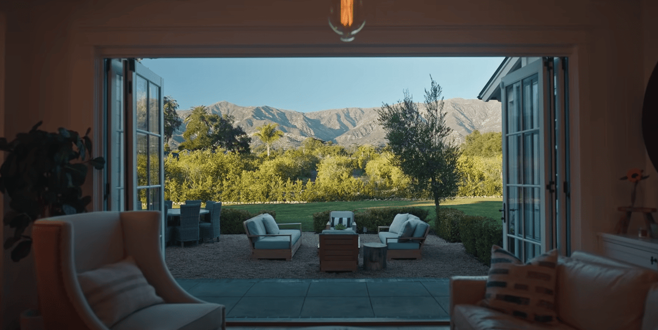  An inviting view from inside a house looking out through wide-open French doors onto a spacious patio and a serene landscape. 