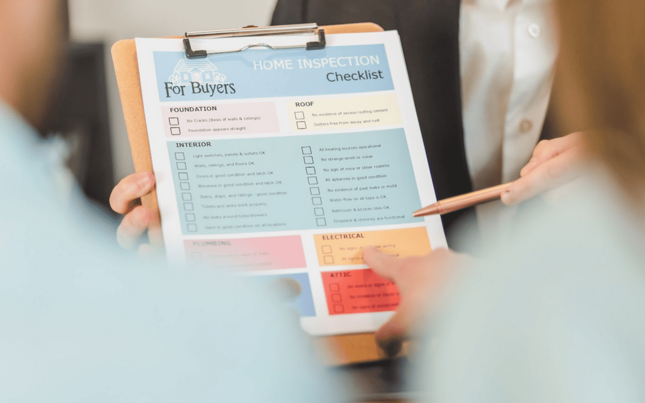  A close-up of a "Home Inspection Checklist For Buyers" document on a clipboard, held by one person with their left hand. 