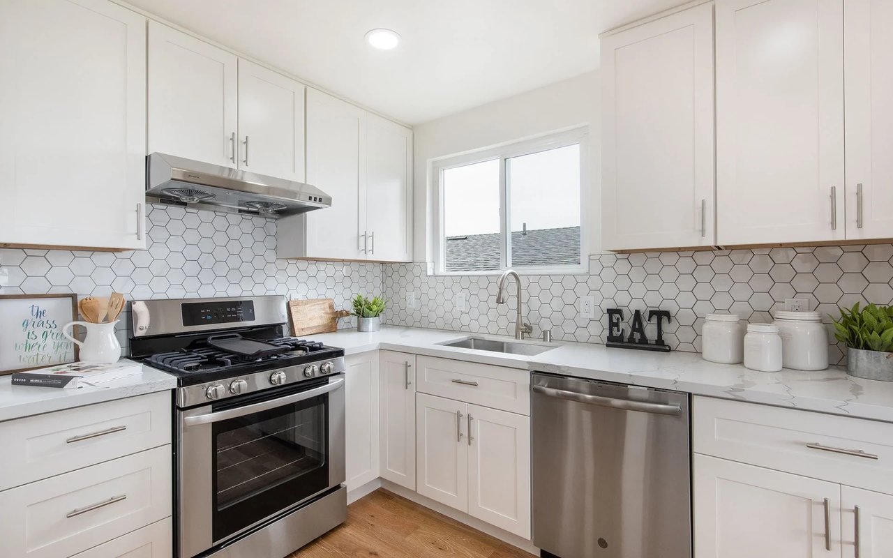 An After photo of a small kitchen in Philadelphia with white cabinets, a stove, microwave, dishwasher, and sink.