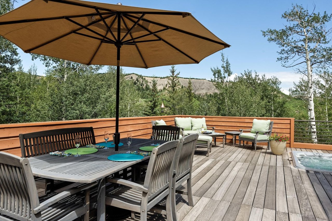 Wooden deck with umbrella-shaded dining set, lounge seating, hot tub, and wooded mountain views.