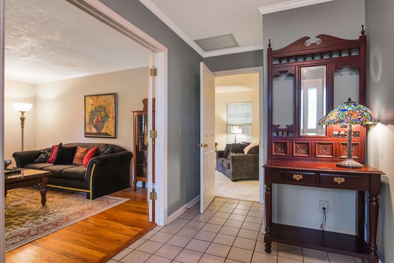 A view of a hallway leading into a living area. The hallway has tiled flooring, and the living area is furnished with a sofa and other furniture.