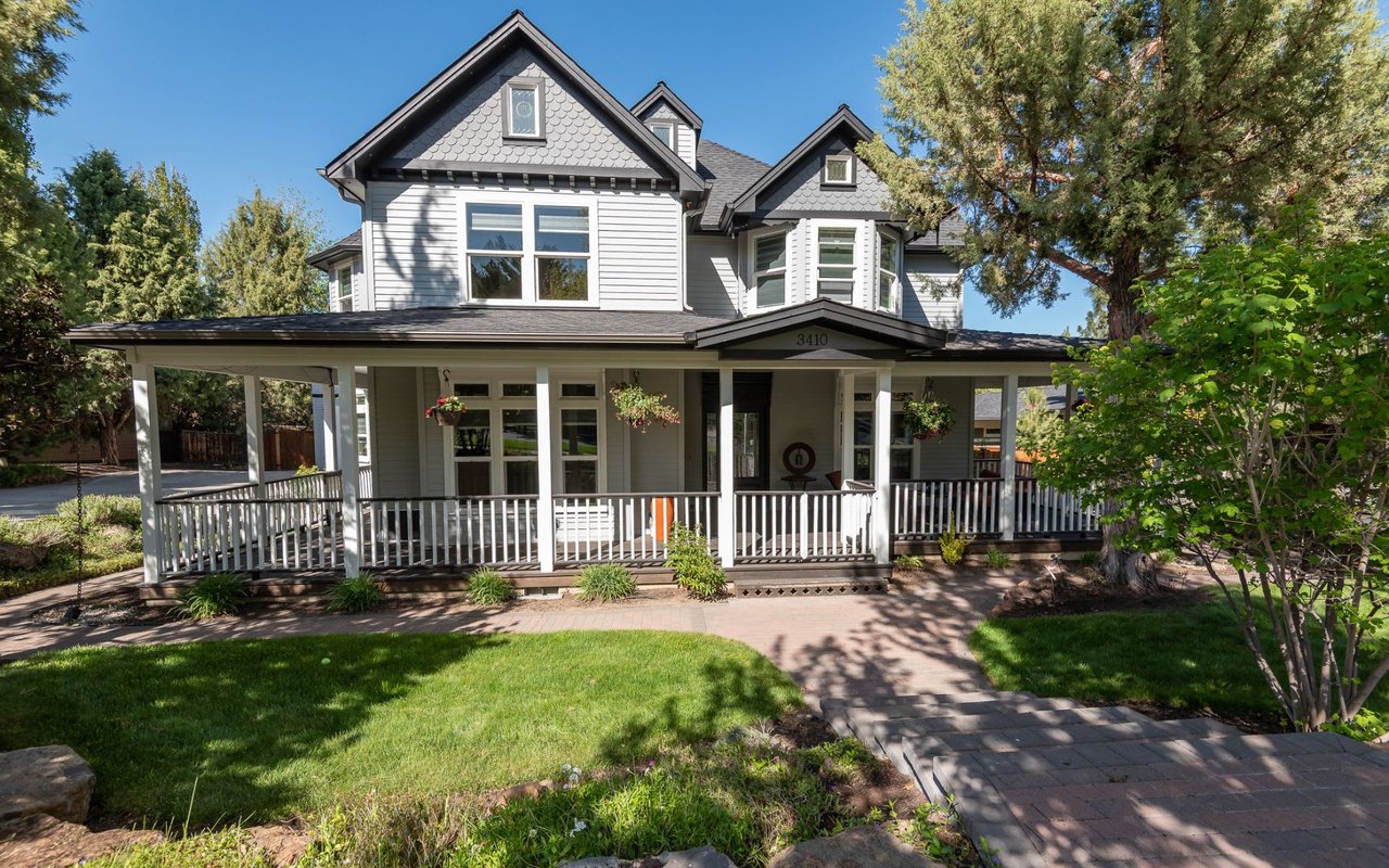 a white and gray home with a green front lawn surrounded by trees