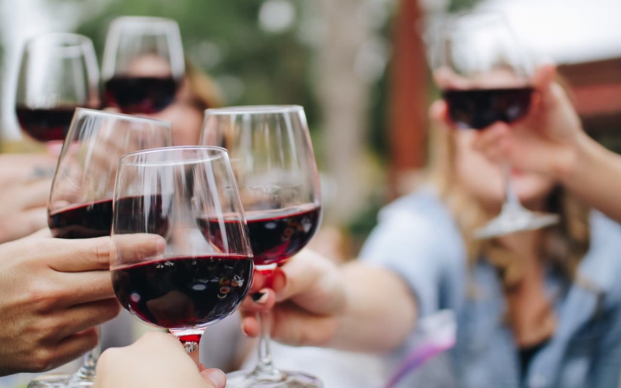 A group of friends raise glasses of red wine in a toast.