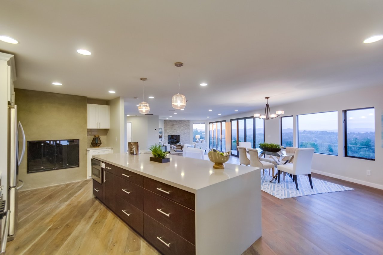 Open-plan kitchen with a large island, modern fireplace, and dining area beside expansive windows.