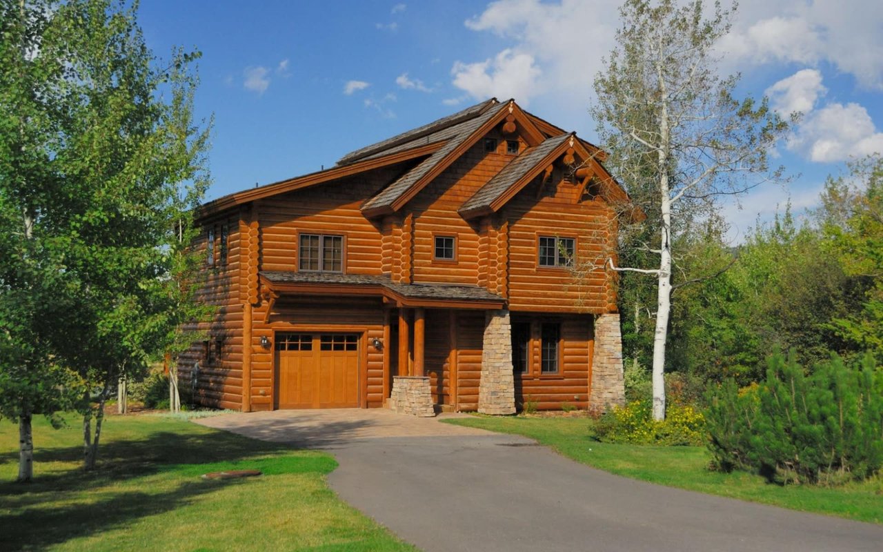 A large log home with a driveway leading up to it.