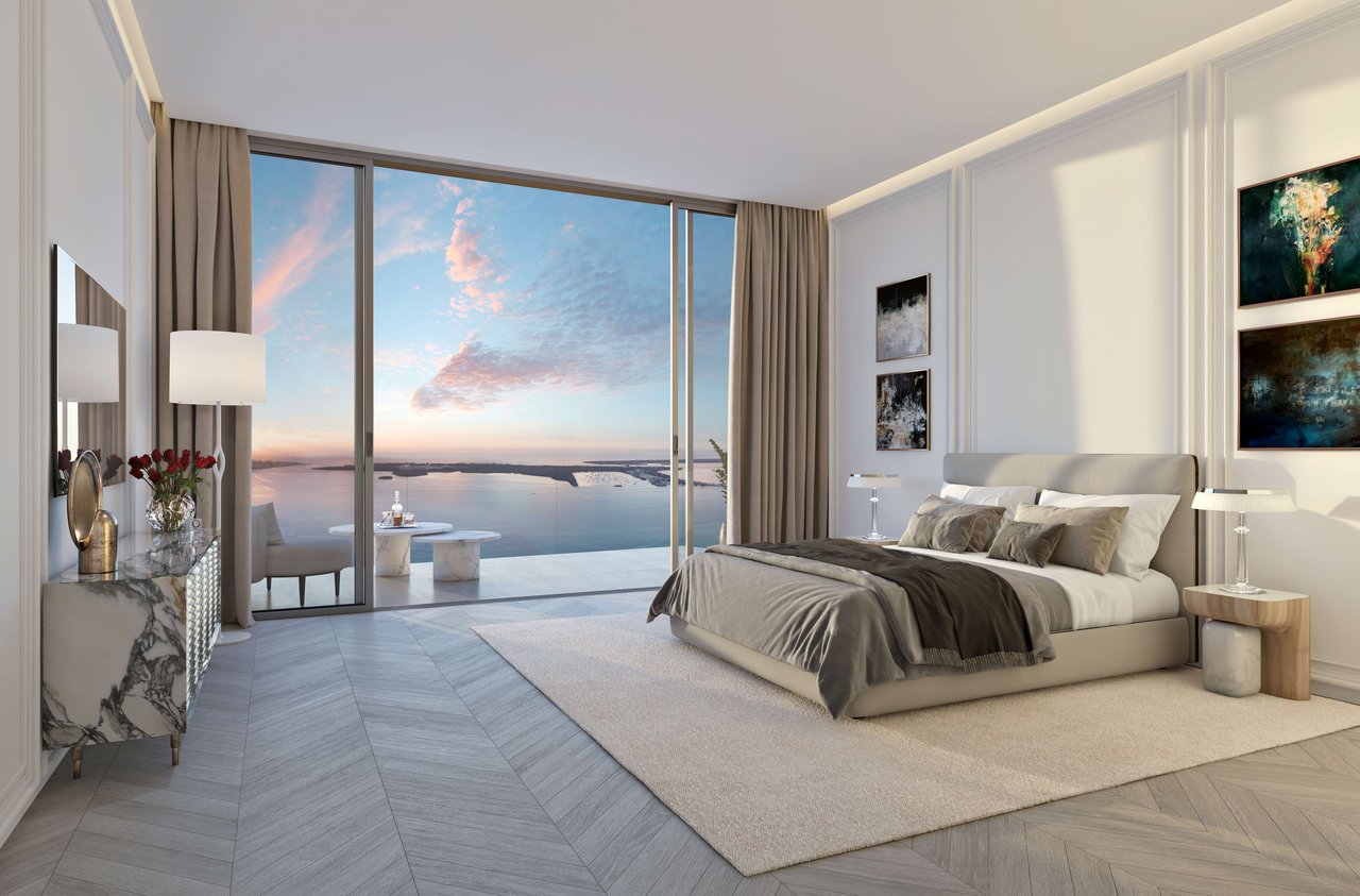 Luxury bedroom with a king bed and floor-to-ceiling windows overlooking calm water at sunset.