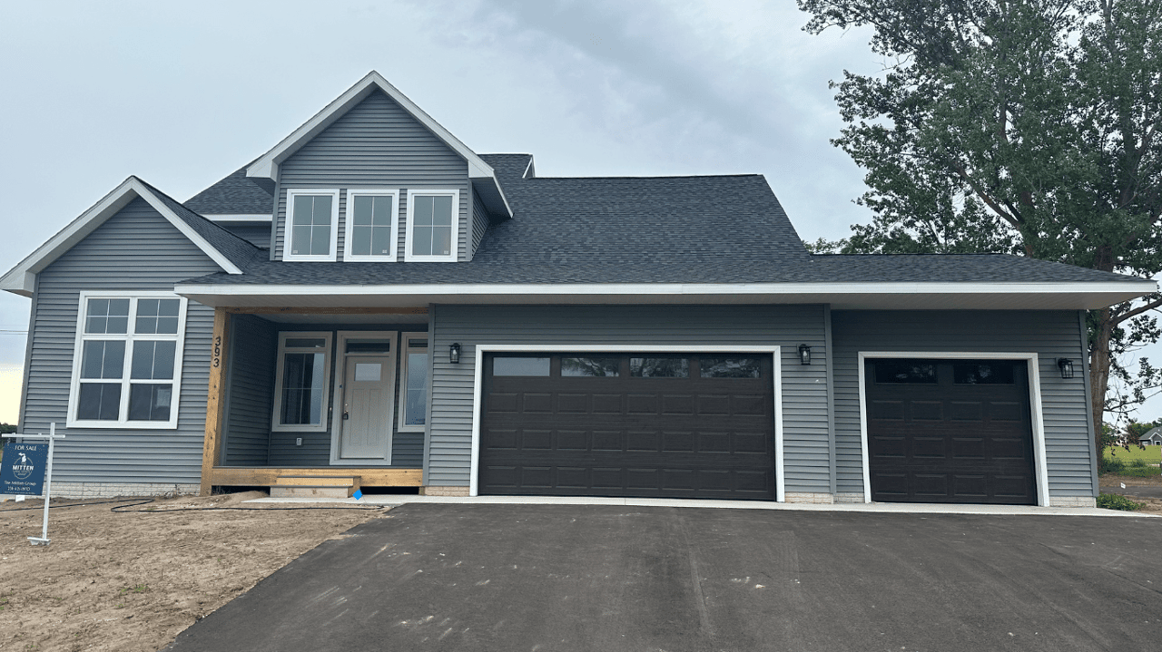 Gray two-story home with a covered porch, two dark garage doors, and a newly paved driveway.