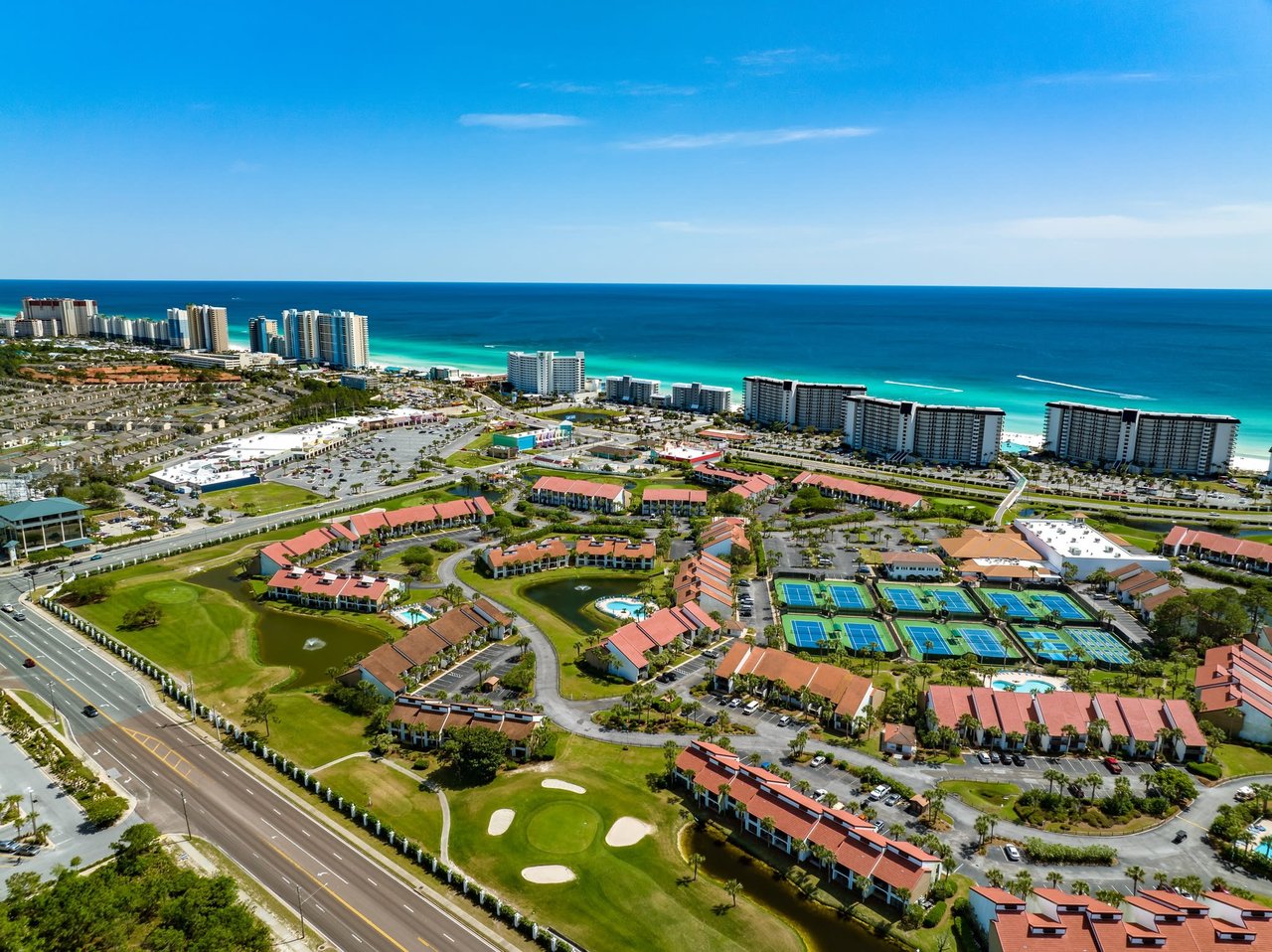 An aerial view of a coastal resort community with a golf course, tennis courts, and numerous buildings.